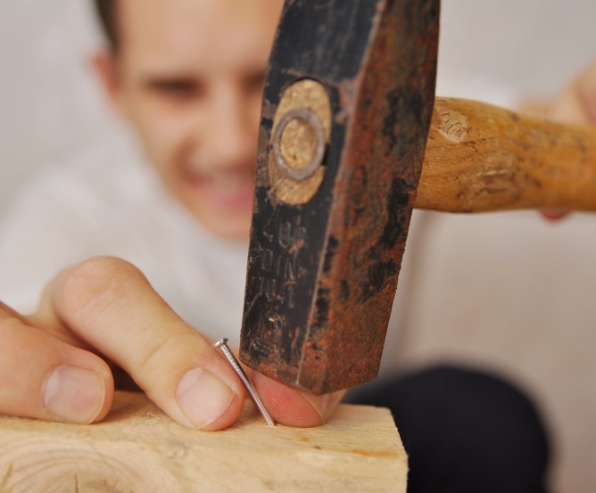 Handwerker schlägt mit Hammer auf den Daumen